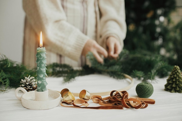 Fazendo uma guirlanda moderna de Natal Vela estilosa como sinos dourados de árvore de abeto e fita na mesa de madeira