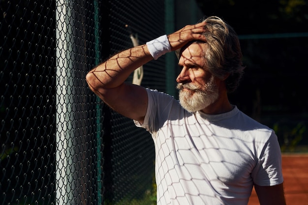 Fazendo uma pausa homem elegante moderno sênior ao ar livre no campo esportivo durante o dia