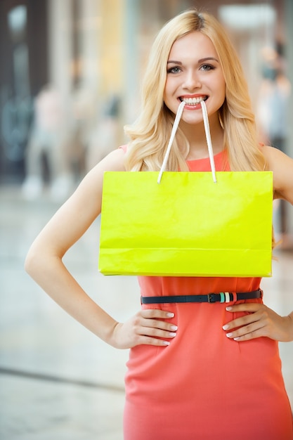 Fazer compras é divertido. Mulher jovem e bonita segurando a sacola de compras na boca e sorrindo