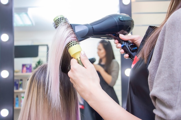 Fazer penteado com secador de cabelo. garota com cabelo comprido loiro em um salão de beleza. barbearia.