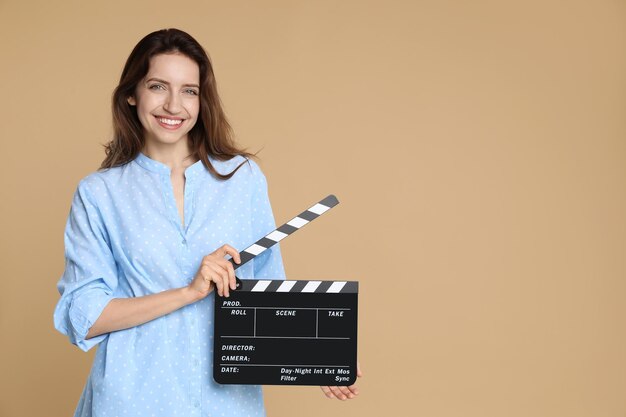 Fazer um filme Mulher sorridente com clapperboard em fundo bege Espaço para texto