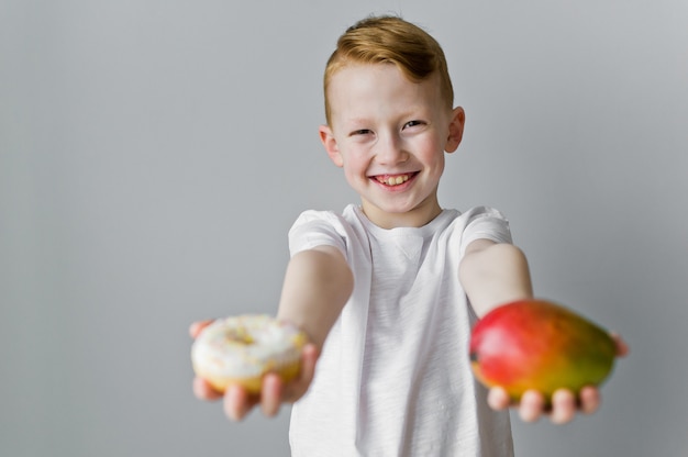 Fazer uma escolha entre alimentos saudáveis e não saudáveis. A criança está segurando um donut e manga