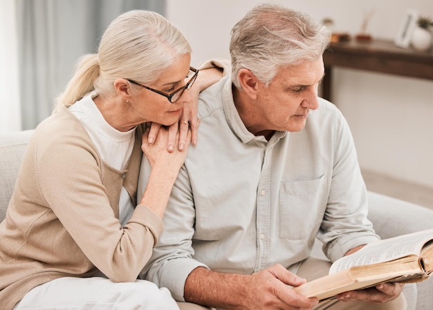 Fe de estudio bíblico y pareja de ancianos con un libro en una sala de estar, lectura relajada y vínculo en casa Adoración a Dios y personas mayores jubiladas con guía de las Escrituras o amor del evangelio y alabanza de Jesús