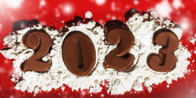 Foto fecha del año nuevo 2023 hecha de chocolate sobre fondo rojo.