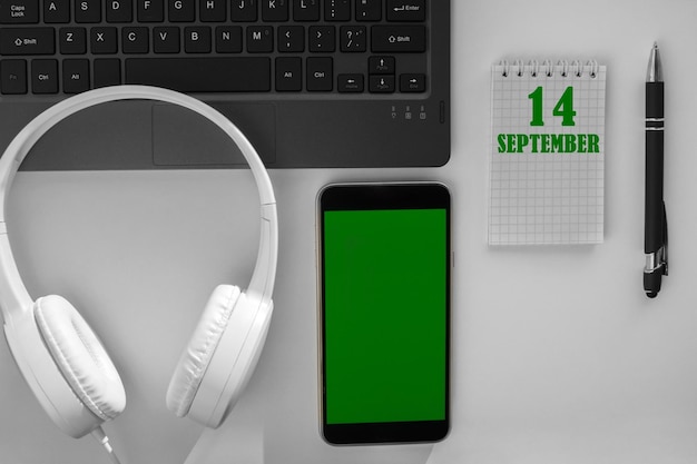 Fecha del calendario en un fondo claro de un escritorio y un teléfono con pantalla verde El 14 de septiembre es el decimocuarto día del mes