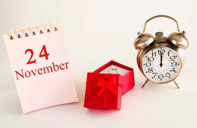 Fecha del calendario sobre fondo claro con caja de regalo roja con anillo y despertador 24 de noviembre