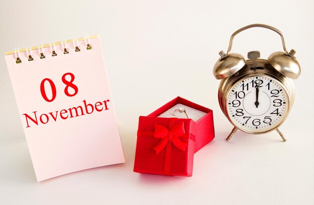 Fecha del calendario sobre fondo claro con caja de regalo roja con anillo y despertador 8 de noviembre