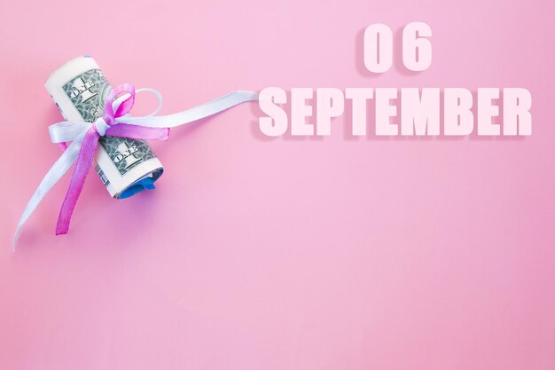 Fecha del calendario sobre fondo rosa con billetes de dólar enrollados fijados por cinta azul rosa 6 de septiembre