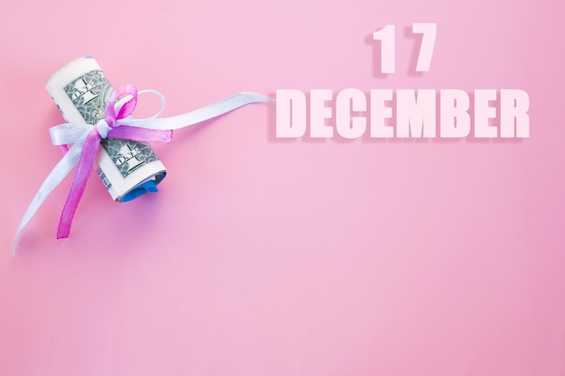 Fecha del calendario sobre fondo rosa con billetes de dólar enrollados fijados por cinta rosa y azul con espacio de copia El 17 de diciembre es el decimoséptimo día del mes