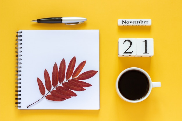 Fecha del calendario, taza de café, bloc de notas con bolígrafo y hojas de otoño