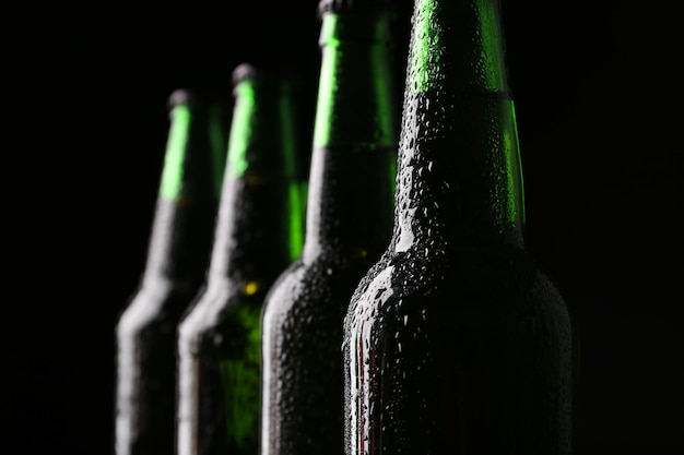 Fecham-se quatro garrafas de vidro verde de cerveja em fundo escuro