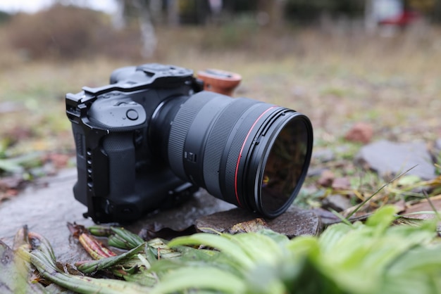 Foto fechamento da câmera fotográfica com lente de zoom no chão na natureza com muitas folhas molhadas