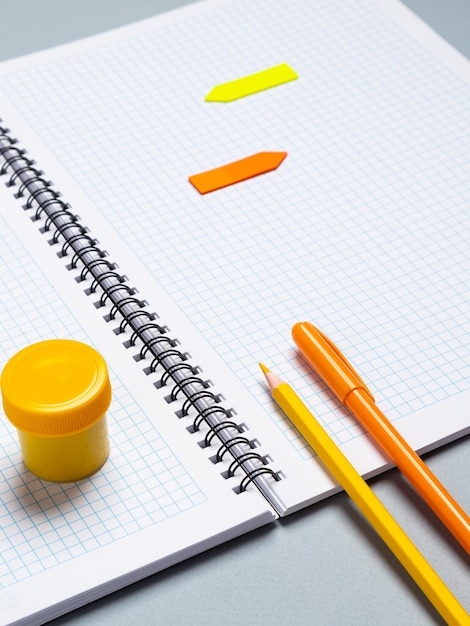 Fechamento de um caderno de papel com folhas em branco, uma caneta, um lápis e um clipe de papel em um fundo azul