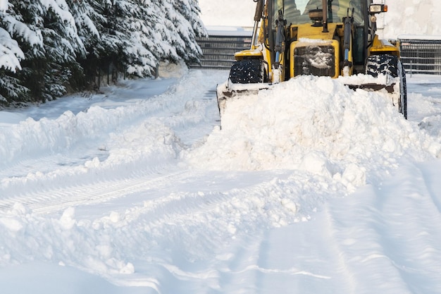 Fechar a estrada de arado de neve durante a remoção de neve de inverno de tempestade remoção de grande trator amarelo