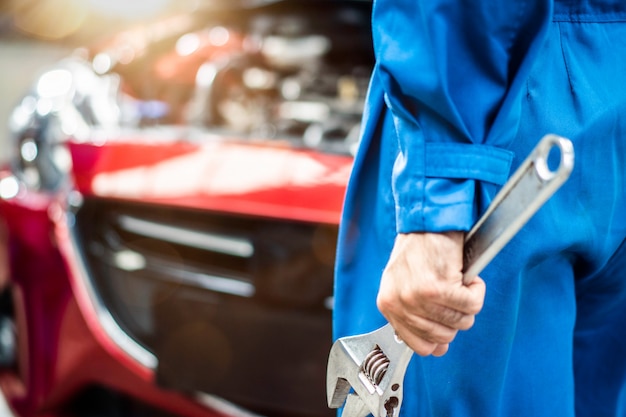 fechar a mão do homem mecânico segurando a ferramenta de equipamento chave na garagem de reparação automóvel