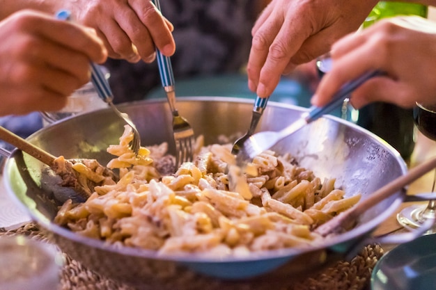 Fechar com vários amigos de mãos diferentes tomando macarrão italiano junto com os garfos para se divertir e curtir a amizade. todo mundo comendo com o mesmo prato. conceito de comida em casa ou restaurante