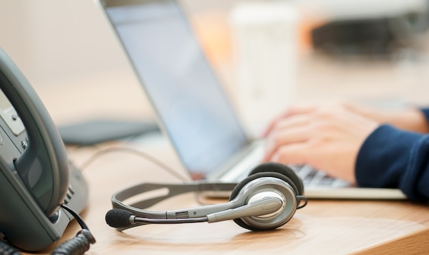 Fechar o fone de ouvido com o tipo de mão de homem trabalhar no teclado do laptop com a mesa de escritório de telefone