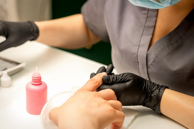 Fechar o mestre de manicure profissional segura a mão feminina do cliente e desinfeta as unhas em um salão de beleza