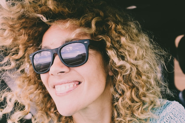 Fechar o retrato da bela jovem adulta caucasiana alegre feliz sorrindo e olhando para a estrada refletida nos óculos de sol durante uma viagem de carro