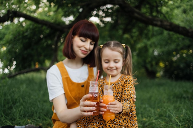 Fechar o retrato da mãe solteira com a filha pequena está envolvida em beber suco