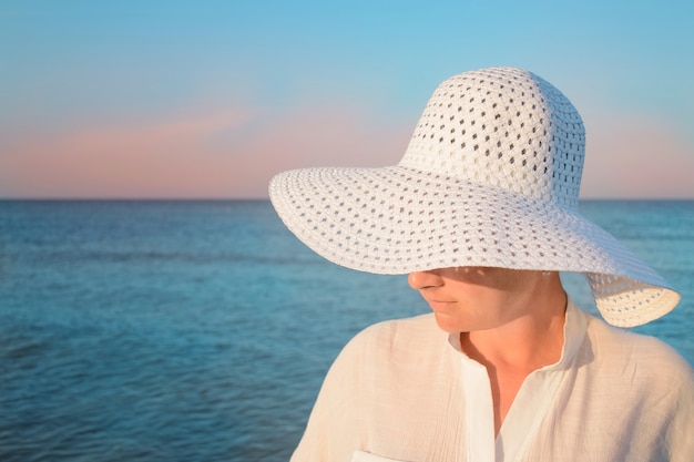 Foto fechar o retrato feminino de jovem com chapéu branco, posando na praia, moda verão praia.