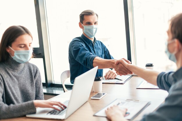 Fechar-se. empresários com máscaras protetoras, apertando as mãos uns dos outros. conceito de proteção à saúde.