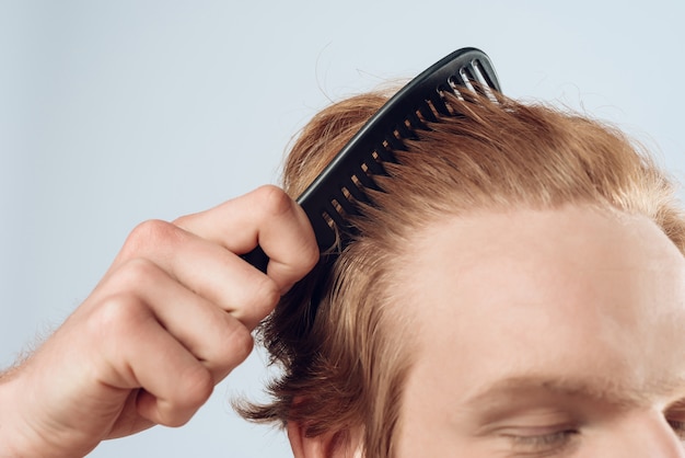 Foto fechar-se. homem de cabelo vermelho satisfeito penteia o cabelo com o pente.