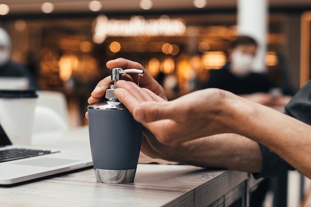 Fechar-se. um homem desinfetando as mãos sentado à mesa de um café