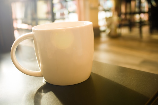 Fechar uma xícara branca de café no efeito de filtro de reflexo de sol de mesa preto