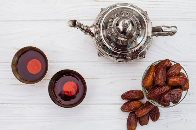 Fechas de frutas con tetera y tazas en mesa.