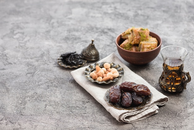Foto fechas jugosas; nueces; té de hierbas y dulces de baklava en un tazón sobre un fondo con textura de hormigón