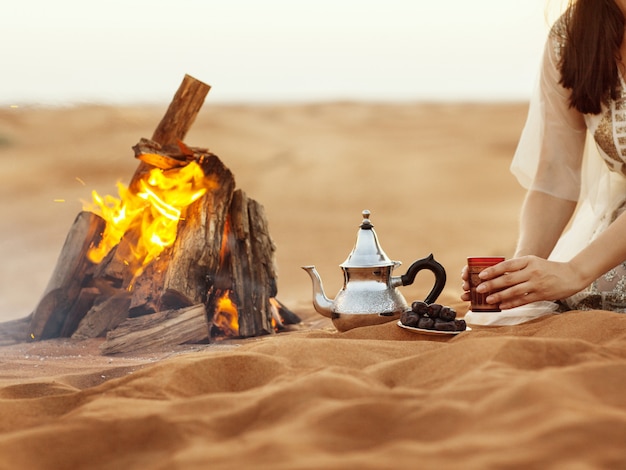 Fechas, tetera, taza con té cerca del fuego en el desierto con un hermoso fondo