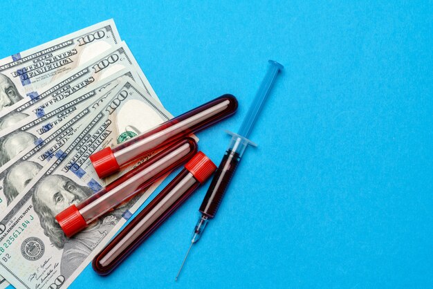Feche 100 notas de dólares americanos e amostra de sangue em tubo de ensaio sobre fundo azul