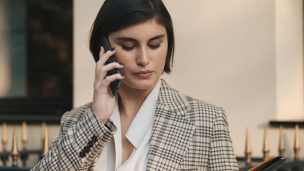 Feche a agente imobiliária atraente falando ao telefone esperando clientes na rua da cidade Tecnologia moderna