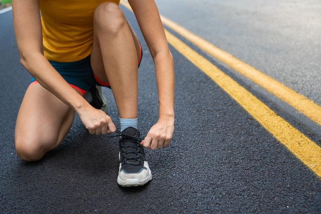 Feche a atleta feminina amarrando cadarços para correr na estrada da floresta. Mulher corredor se preparando.