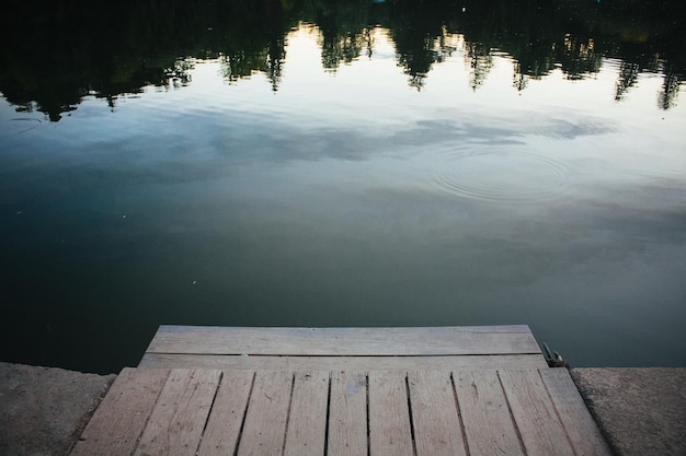 Feche a doca do lago de madeira em frente à floresta refletindo na foto do conceito de água