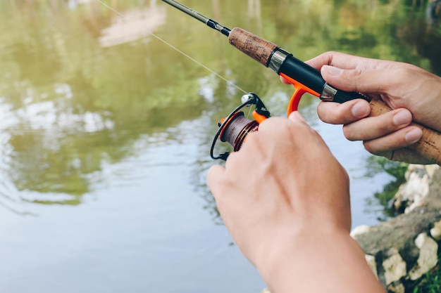 Feche a fiação com o carretel de pesca no gancho de pesca manual na linha com a isca na mão esquerda contra o fundo da água