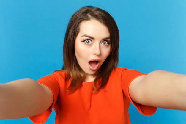 Feche a foto da jovem em roupas laranja vermelhas, olhando para a câmera posando fazendo selfie tiro isolado sobre fundo azul na moda, retrato de estúdio. Conceito de moda de estilo de vida de pessoas. Mock up espaço de cópia.