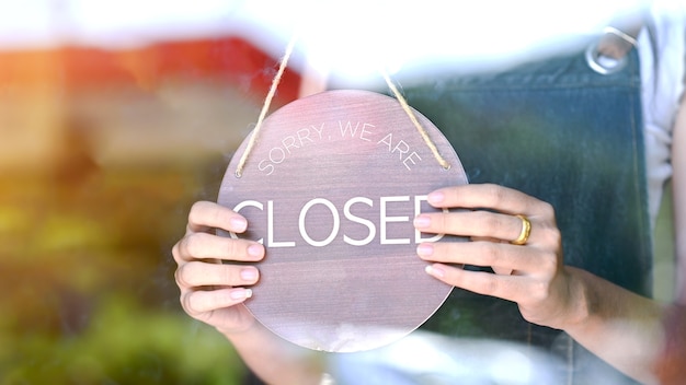 Foto feche a foto da mão de uma mulher virando a placa de sinalização fechada na porta de vidro em um café e restaurante