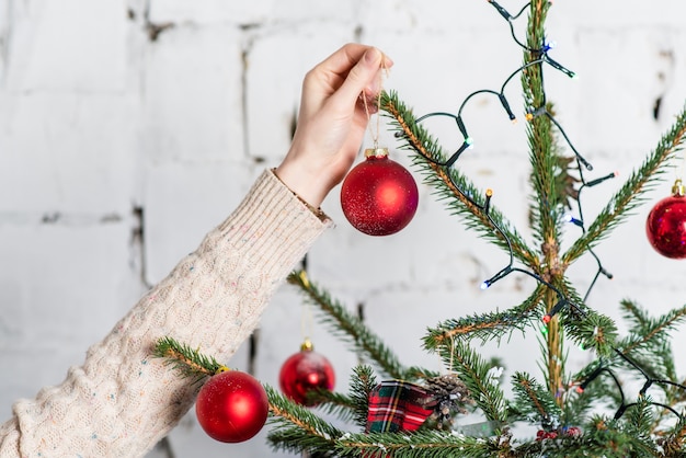 Feche a foto da mão que pendura as bolas vermelhas na árvore de natal