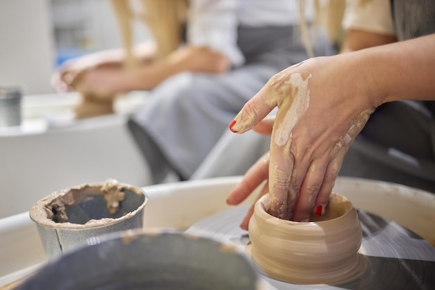 Feche a foto das mãos de artesãos trabalhando com argila no estúdio de cerâmica