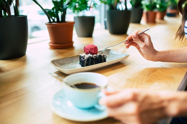 Feche a foto das mãos femininas enquanto ela come bolo de chocolate com sorvete de frutas e café no café