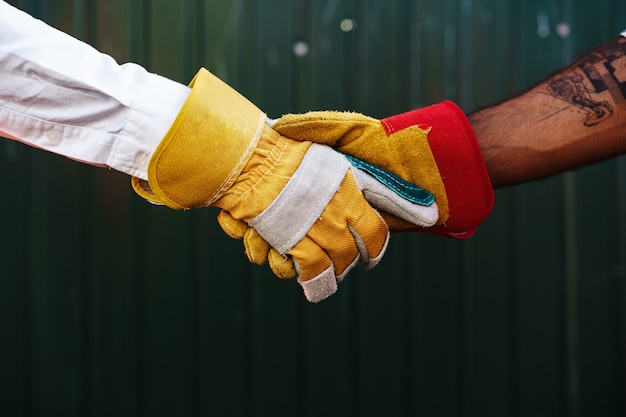 Feche a foto de dois construtores masculinos em trajes de trabalho apertando as mãos