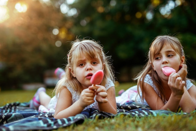 Feche a foto de duas garotas loiras desfrutando de tomar sorvete em um piquenique