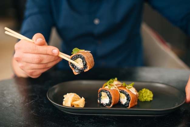 Feche a foto de um homem comendo sushi em um prato.