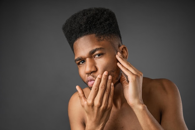 Feche a foto de um jovem afro-americano à procura de acnes no rosto Conceito de cuidados com a pele