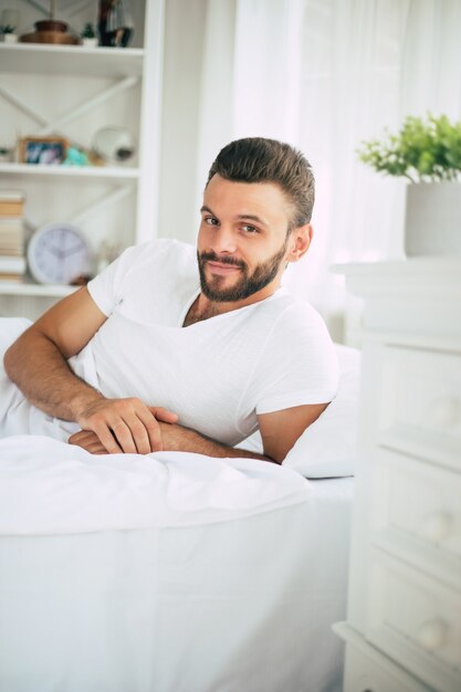 Feche a foto de um jovem barbudo deitado na cama e relaxando pela manhã