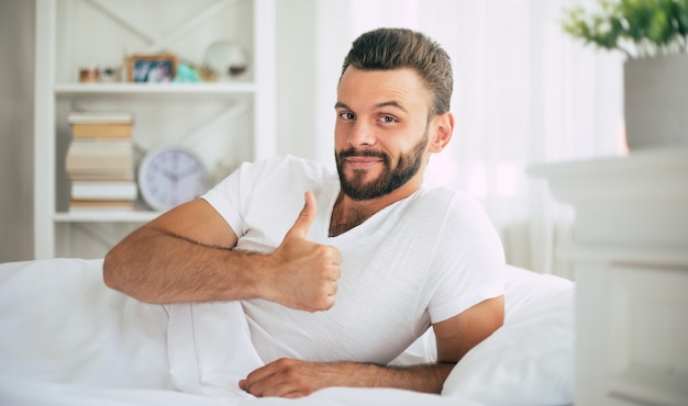 Feche a foto de um jovem barbudo deitado na cama e relaxando pela manhã