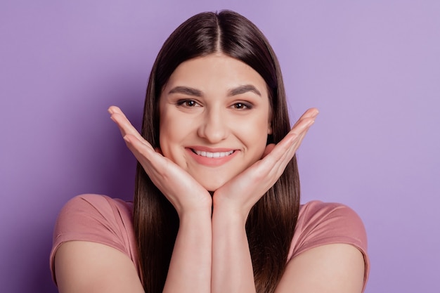 Feche a foto de uma bela garota atraente feliz sorriso positivo com as mãos tocando o queixo isolado sobre o fundo de cor violeta