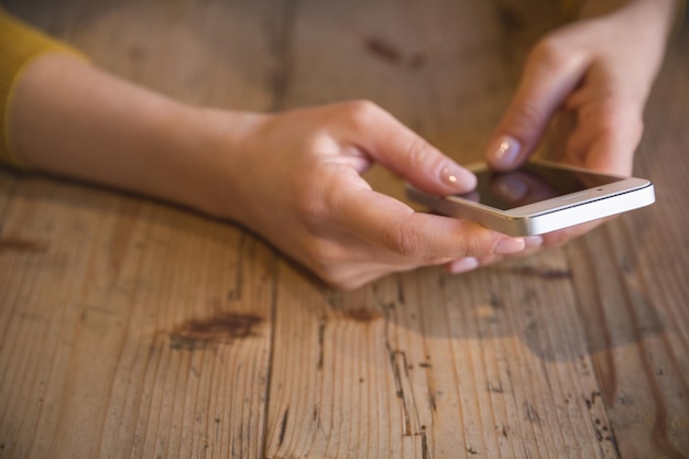 Feche a foto de uma bela jovem sentada confortável na mesa de madeira Garota usando smartphone com tela sensível ao toque Digitando no telefone